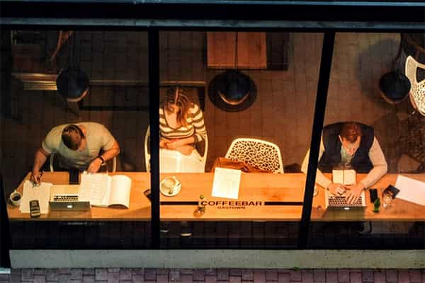 view through a cafe window where customers are seated reading and working on laptops